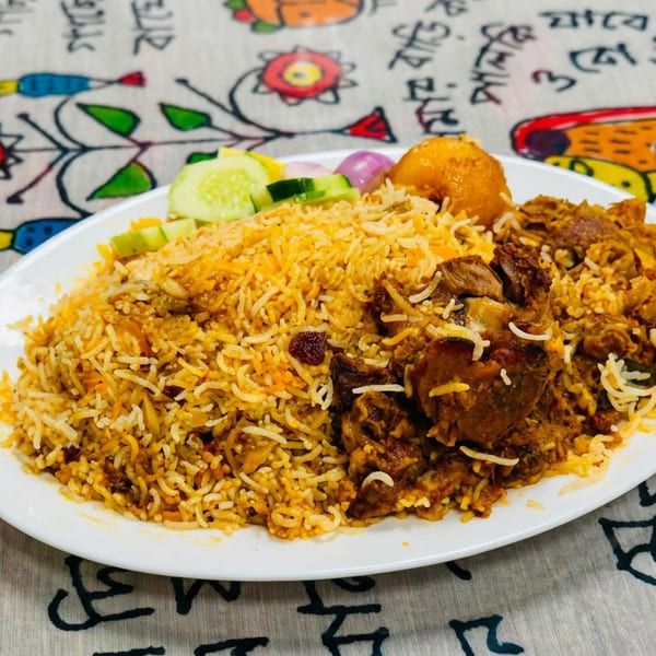 Plate of spiced biryani rice with chicken, fried egg, cucumber, and onion salad on colorful patterned fabric.
